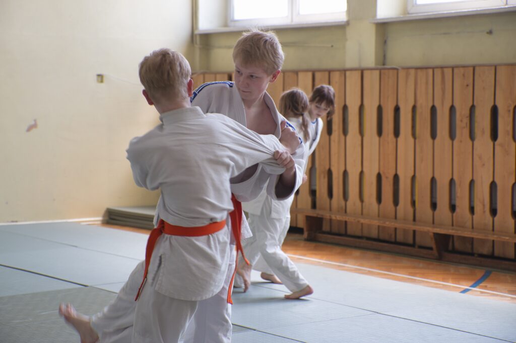 Na zdjęciu widzimy salę gimnastyczną na której są przedstawione chwyty karate przez uczniów