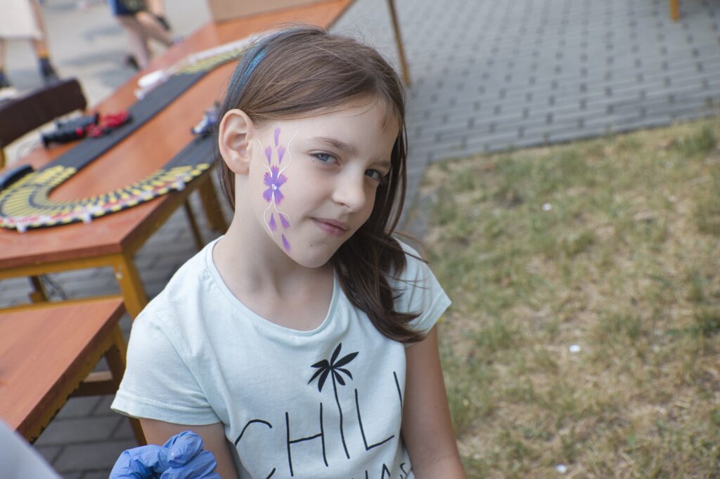Na zdjęciu widzimy uśmiechniętą dziewczynkę z namalowanym tatuażem na twarzy