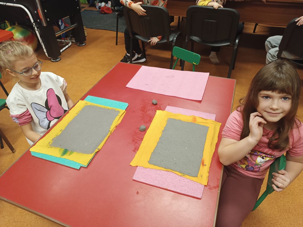 dzieci siedzą przy stoliku na którym jest zrobiony przez nich papier