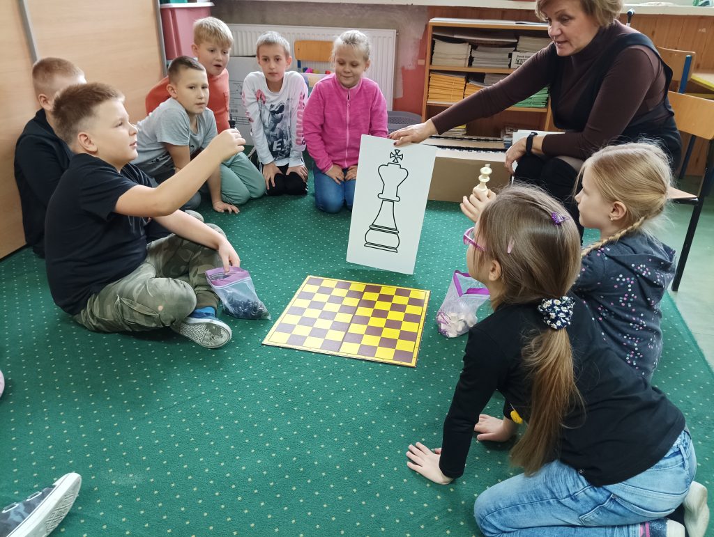 uczniowie grają w szachy, nauczyciel coś tłumaczy