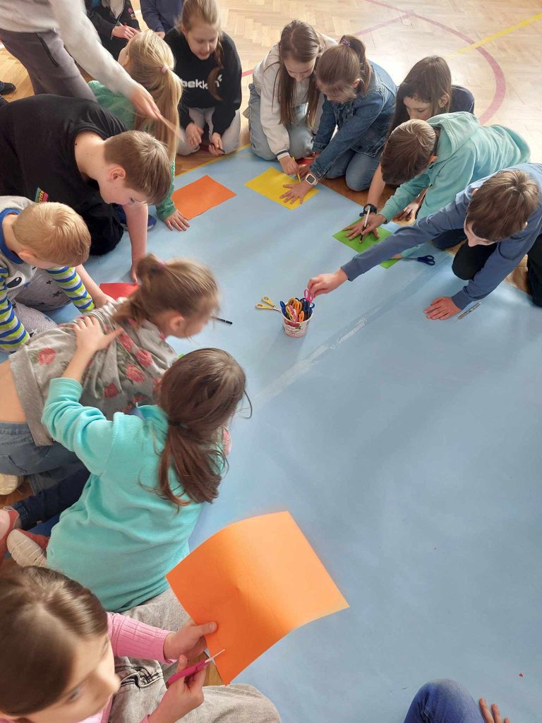 zdjęcie przedstawia jak dzieci wykonują pracę na podłodze na niebieskim papierze