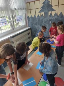 Zdjęcie przedstawia jak młodsi uczniowie losują hasła z niebieskich kopert