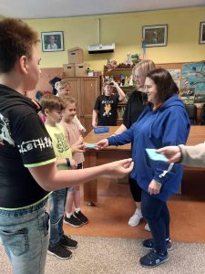 Zdjęcie przedstawia jak uczniowie rozdają niebieskie koperty pracownikom jordanka