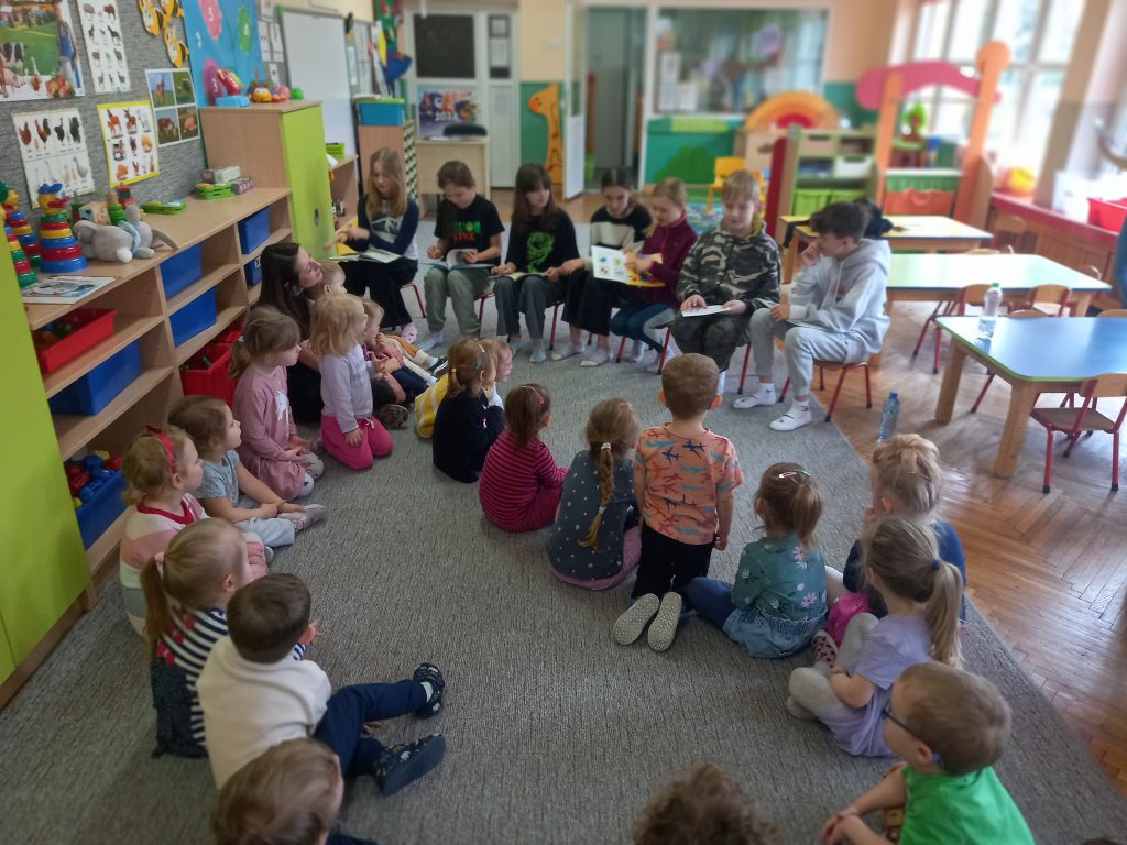 zdjęcie przedstawia uczniów siedzących w kole słuchających czytających uczniów