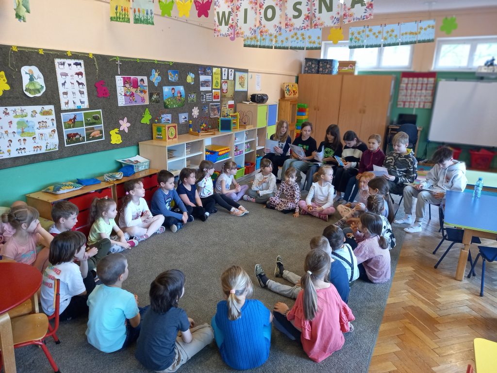 zdjęcie przedstawia dzieci siedzące w kole słuchających uczniów
