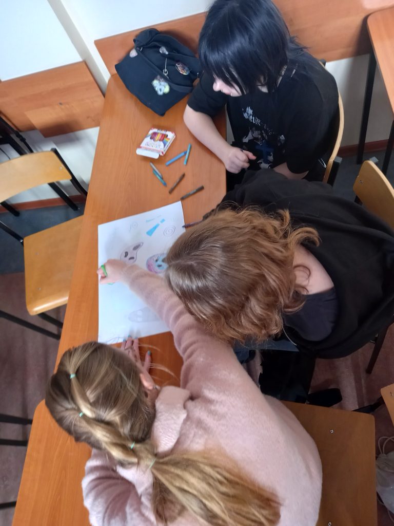 Zdjęcie przedstawia jak uczennice pracują w ławkach nad plakatem.