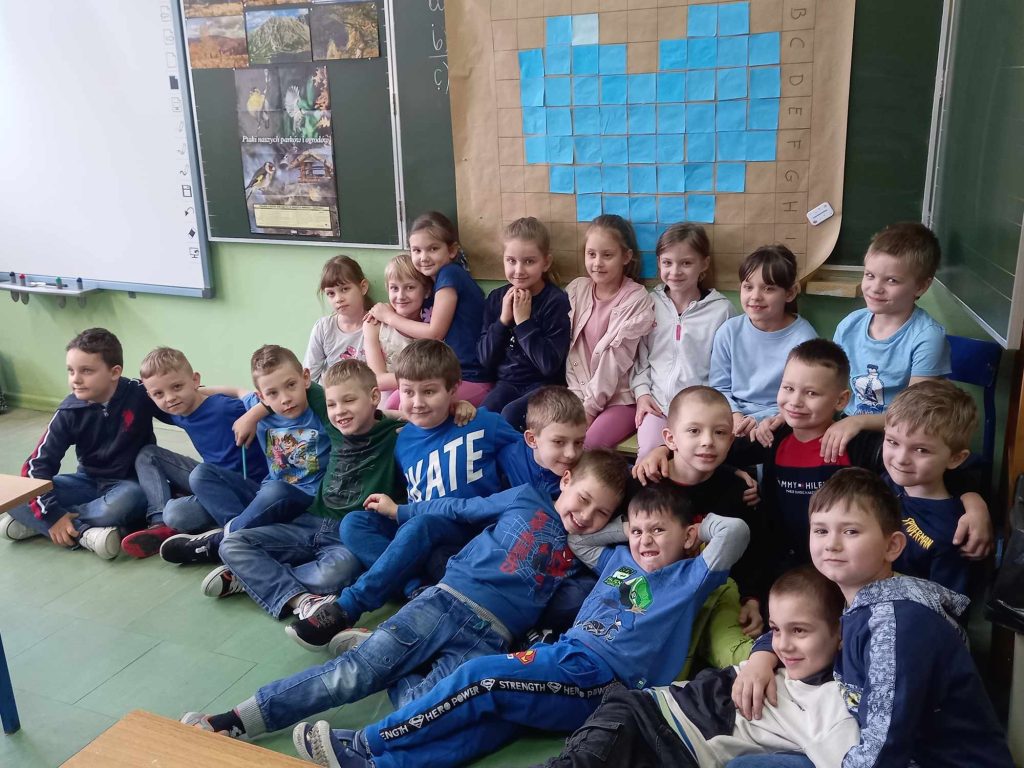 zdjęcie przedstawia grupowe zdjecie uczniów na tle niebieskiego serca