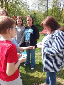 Zdjęcie przedstawia jak pani w parku czyta hasło motywacyjne przekazane jej przez ucznia