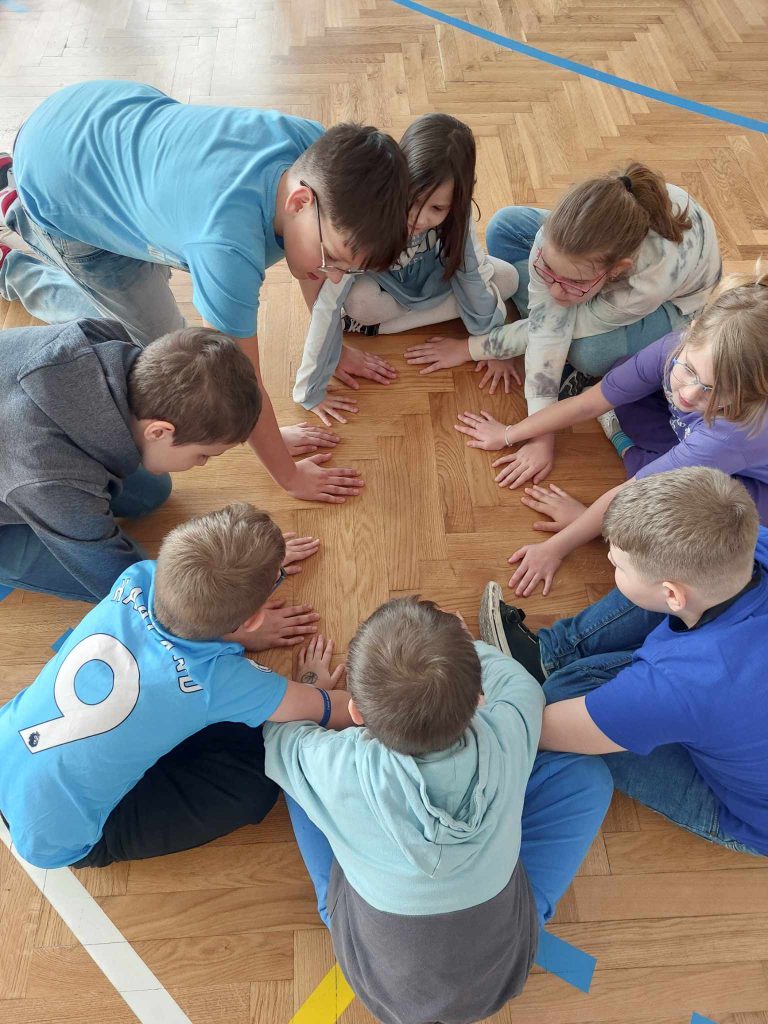 zdjęcie przedstawia jak uczniowie siedzą w kole na podłodze