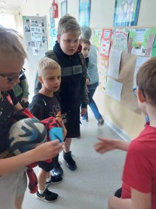 Zdjęcie przedstawia jak uczeń wręcza innemu uczniowi niebieską kopertę