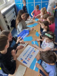 Zdjęcie przedstawia uczniów przed stolikiem z hasłami motywacyjnymi o autyźmie