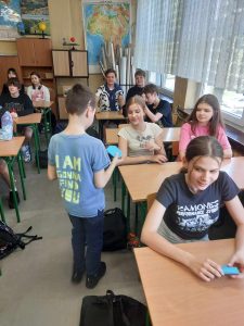 Zdjęcie przedstawia widzimy jak uczeń rozdaje niebieską kopertę uczniom.