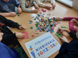 na zdjeciu widzimy rączki dzieci i klocki, widać również plakat z napisem niebieskie igrzyska 2 kwietnia