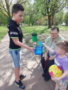 Zdjęcie przedstawia jak uczeń rozdaje hasła motywacyjne w parku