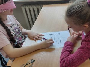 Zdjęcie przedstawia jak uczennica rozwiązuje zadanie z zamkniętymi oczyma kierowana przez koleżankę