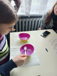 Uczennica przelewa wodę łyżeczką na czas.