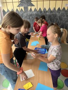 Zdjęcie przedstawia jak młodsza uczennica trzyma hasło na karteczce które wylosowała