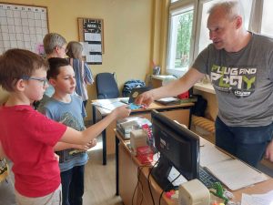 Zdjęcie przedstawia uczniów dających pracownikom niebieskie koperty z hasłem