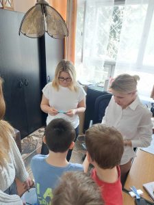 Zdjęcie przedstawia uczniów dających nauczycielom niebieskie koperty z hasłem