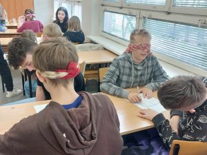 Zdjęcie przedstawia jak uczniowie z zamkniętymi oczyma rozwiązują zadania