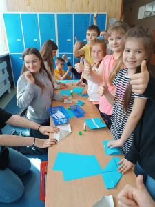 Zdjęcie przedstawia uczniów przy stoliku do pobrania haseł, trzymają kciuki w górze