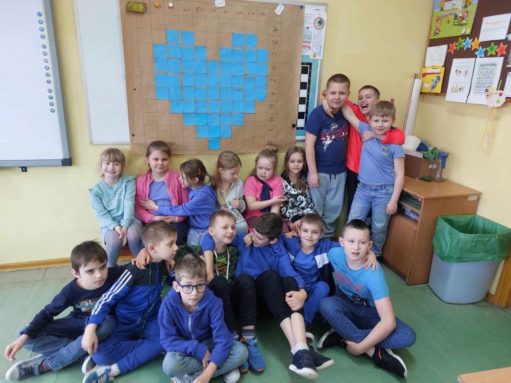 zdjęcie przedstawia zdjecie grupowe klasy na tle niebieskiego serca