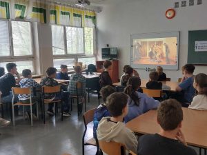 Zdjęcie przedstawia uczniów siedzących w ławkach i oglądających film