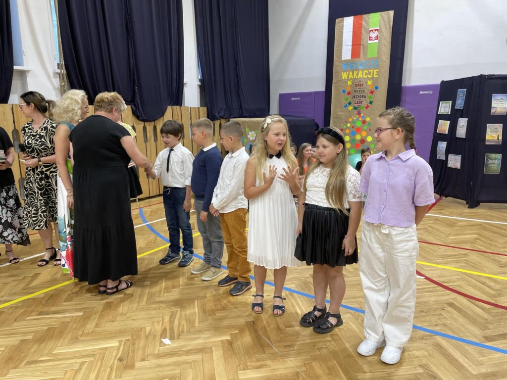 grupa uczniów ma wręczane nagrody na środku sali gimnastycznej