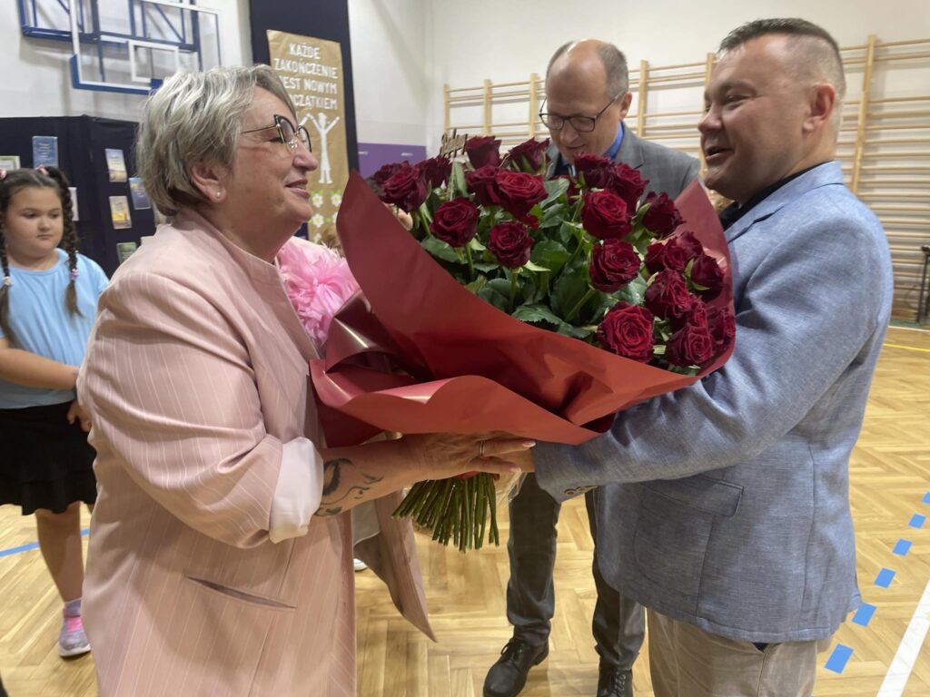 dwóch mężczyzn wręcza bukiet czerwonych róż Pani Dyrektor 