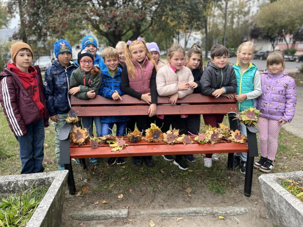 zdjęcie grupowe klasy, stoją przed ławką, na ławce stworki zrobione z liści