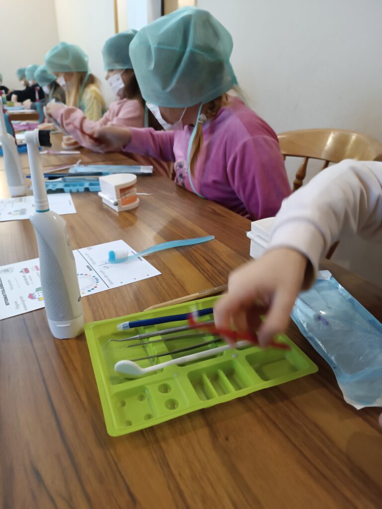 warsztaty stomatologiczne, dzieci w ławkach myją zęby i wykonują inne czynności związane z zawodem dentysty