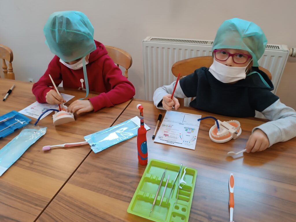 warsztaty stomatologiczne, dzieci w ławkach myją zęby i wykonują inne czynności związane z zawodem dentysty