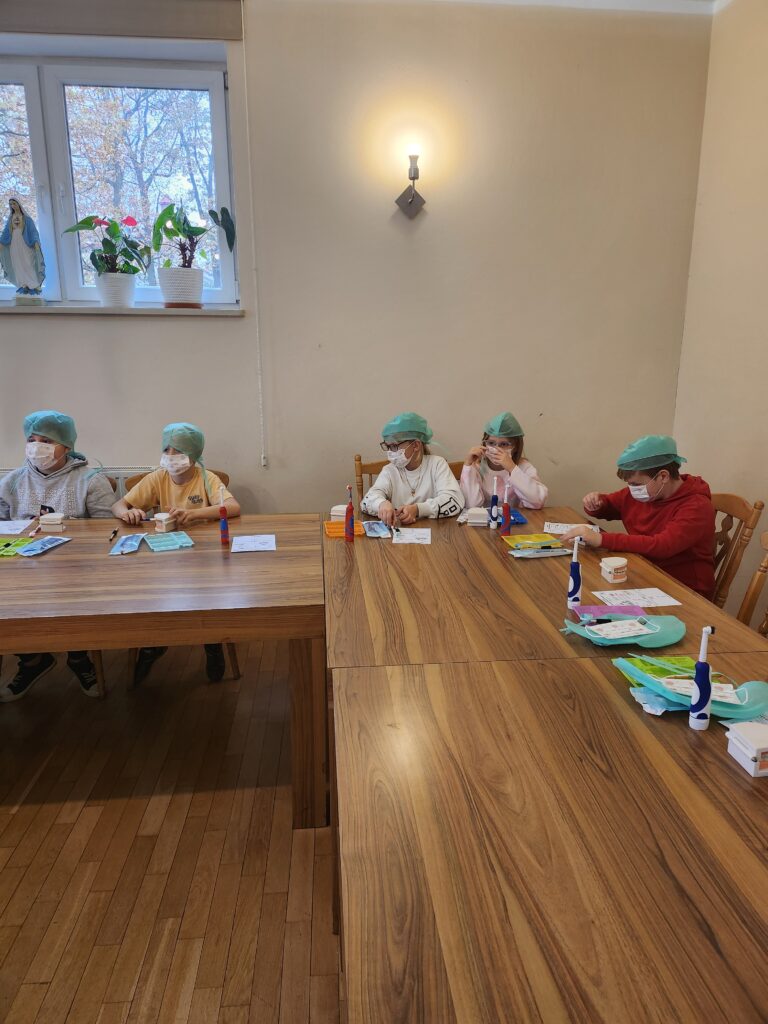 warsztaty stomatologiczne, dzieci w ławkach myją zęby i wykonują inne czynności związane z zawodem dentysty