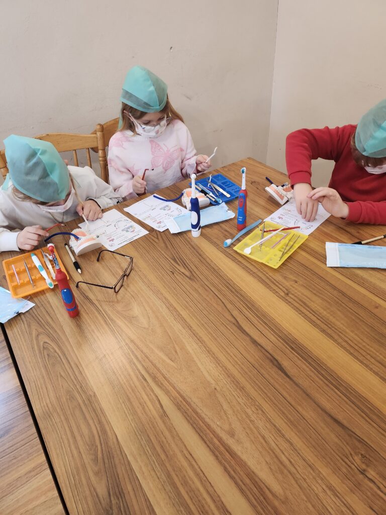 warsztaty stomatologiczne, dzieci w ławkach myją zęby i wykonują inne czynności związane z zawodem dentysty