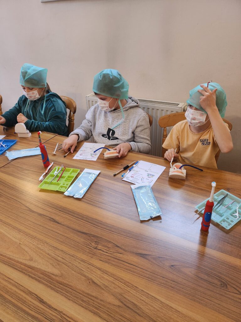 warsztaty stomatologiczne, dzieci w ławkach myją zęby i wykonują inne czynności związane z zawodem dentysty