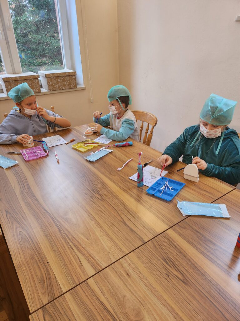 warsztaty stomatologiczne, dzieci w ławkach myją zęby i wykonują inne czynności związane z zawodem dentysty