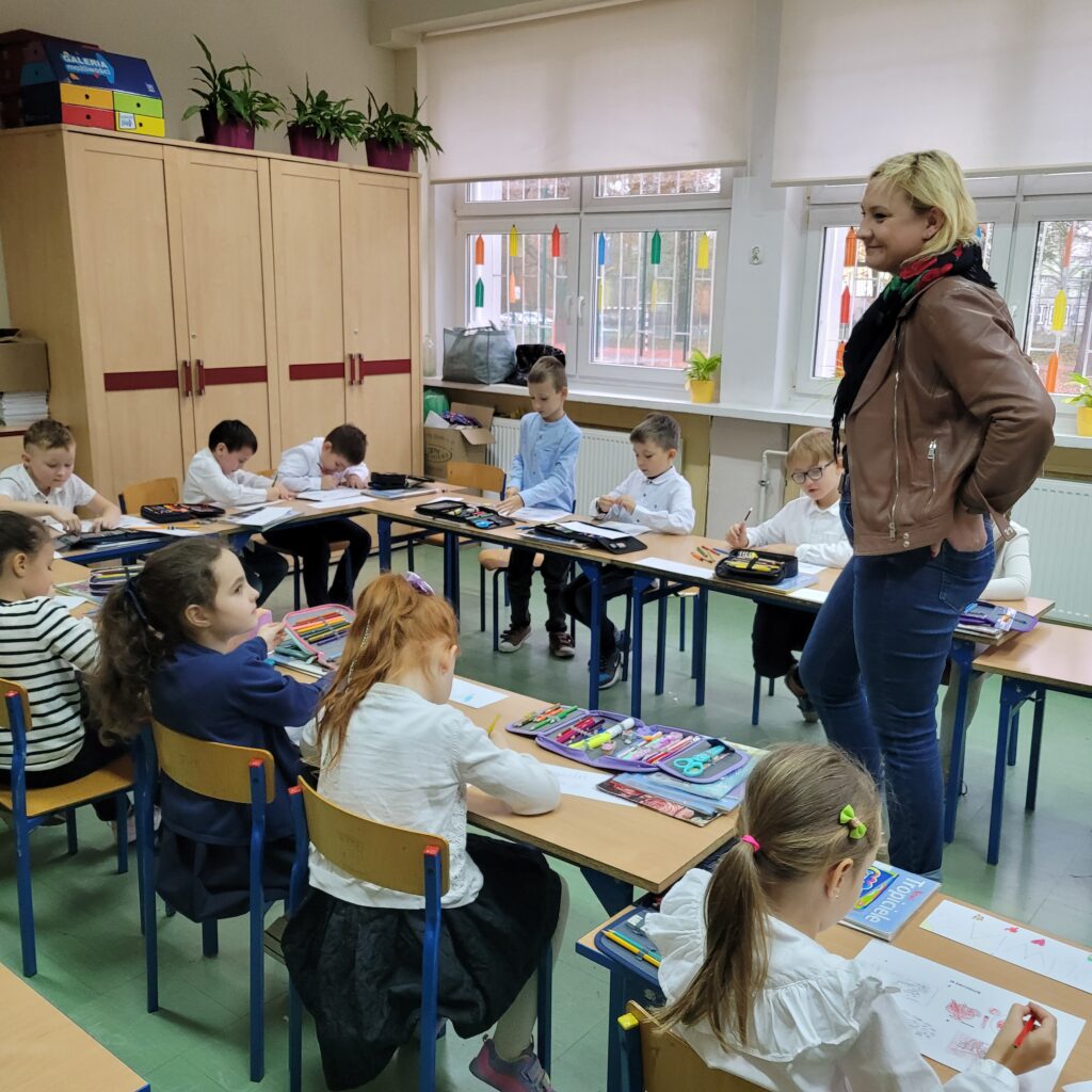 dzieci wykonują kartę pracy w ławkach, pani się do nich uśmiecha