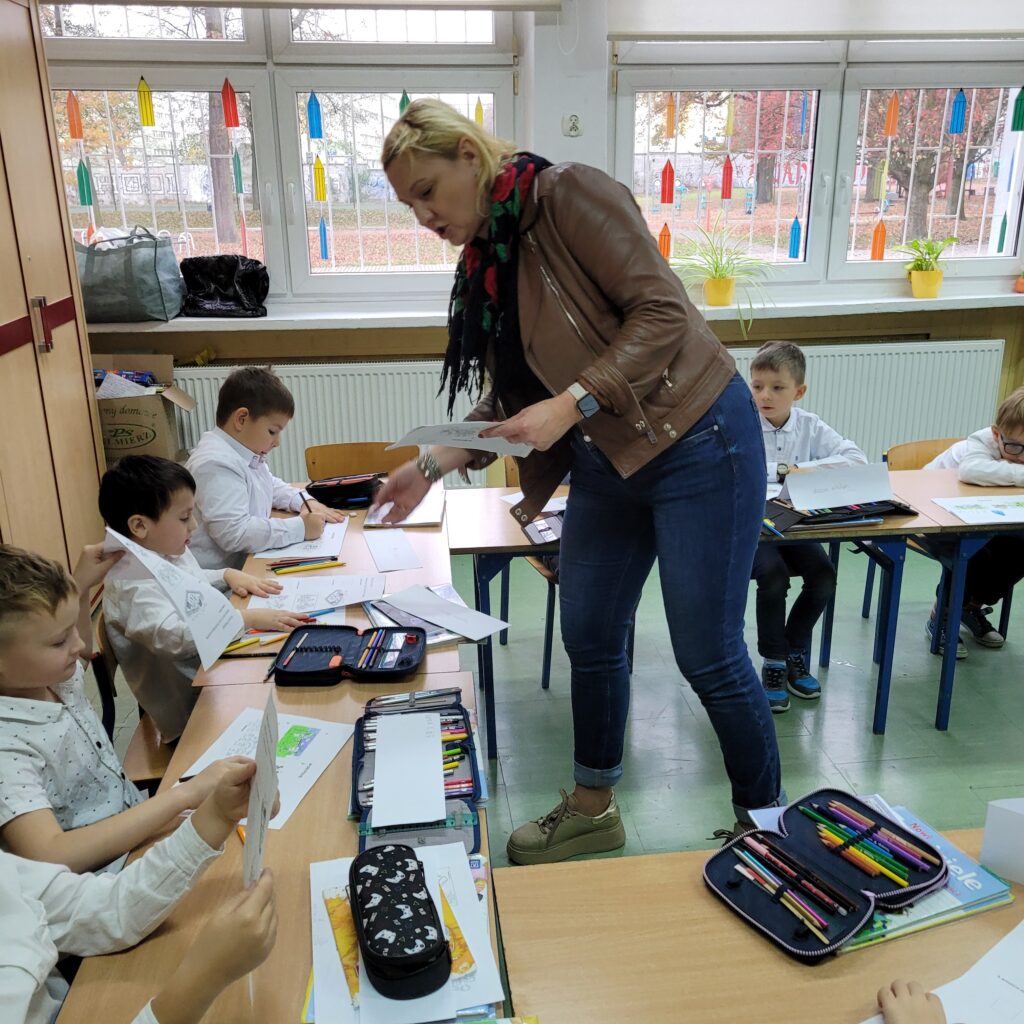 pani rozdaje uczniom siedzącym w ławkach karty pracy