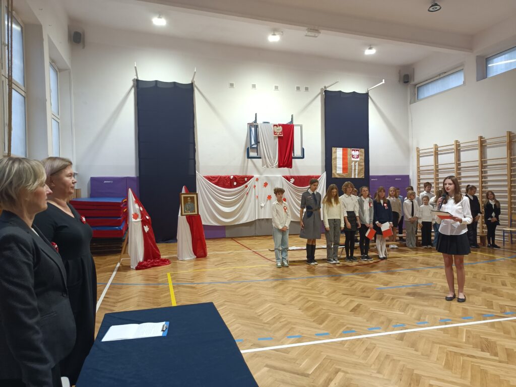 uczniowie stoją na przedstawieniu, z boku widać dyrekcje