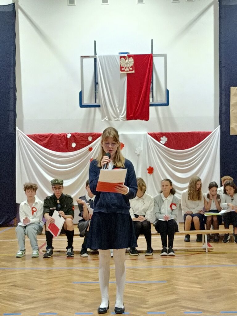 uczennica czyta wiersz, trzyma zeszyt biało czerwony.