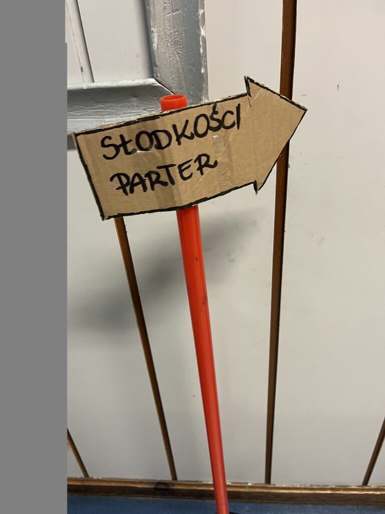 Na zdjęciu widać znak kierujący do stoiska ze słodkościami. 