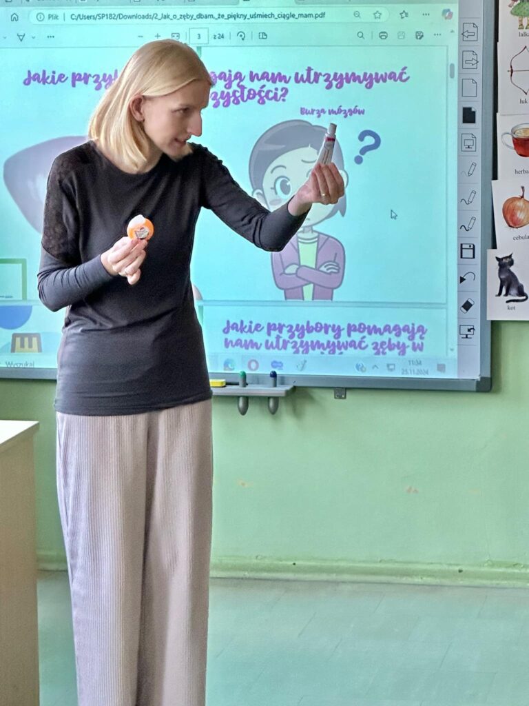zdjęcie nauczycielki tłumaczącej coś dzieciom i w tle prezentacja na ekranie