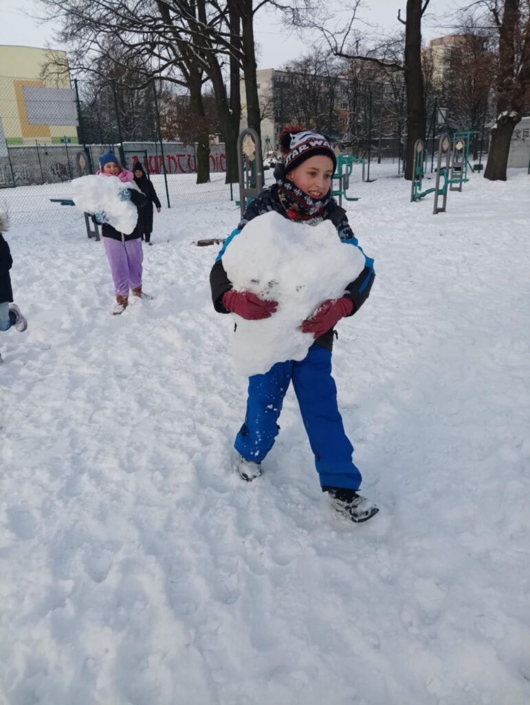 dziecko trzyma kulę śnieżną w rękach, za nim kolejne z kulą