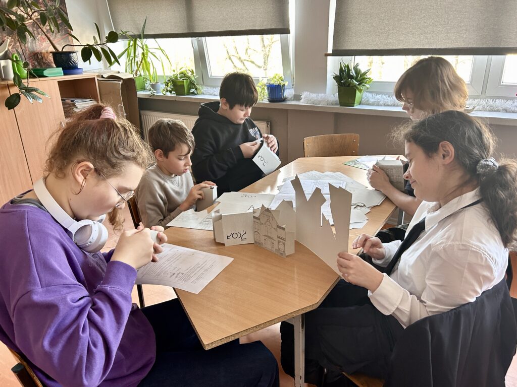dzieci siedzą przy stolikach i budują z papieru