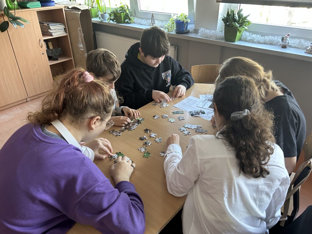 dzieci siedzą przy ławkach i układają puzzle