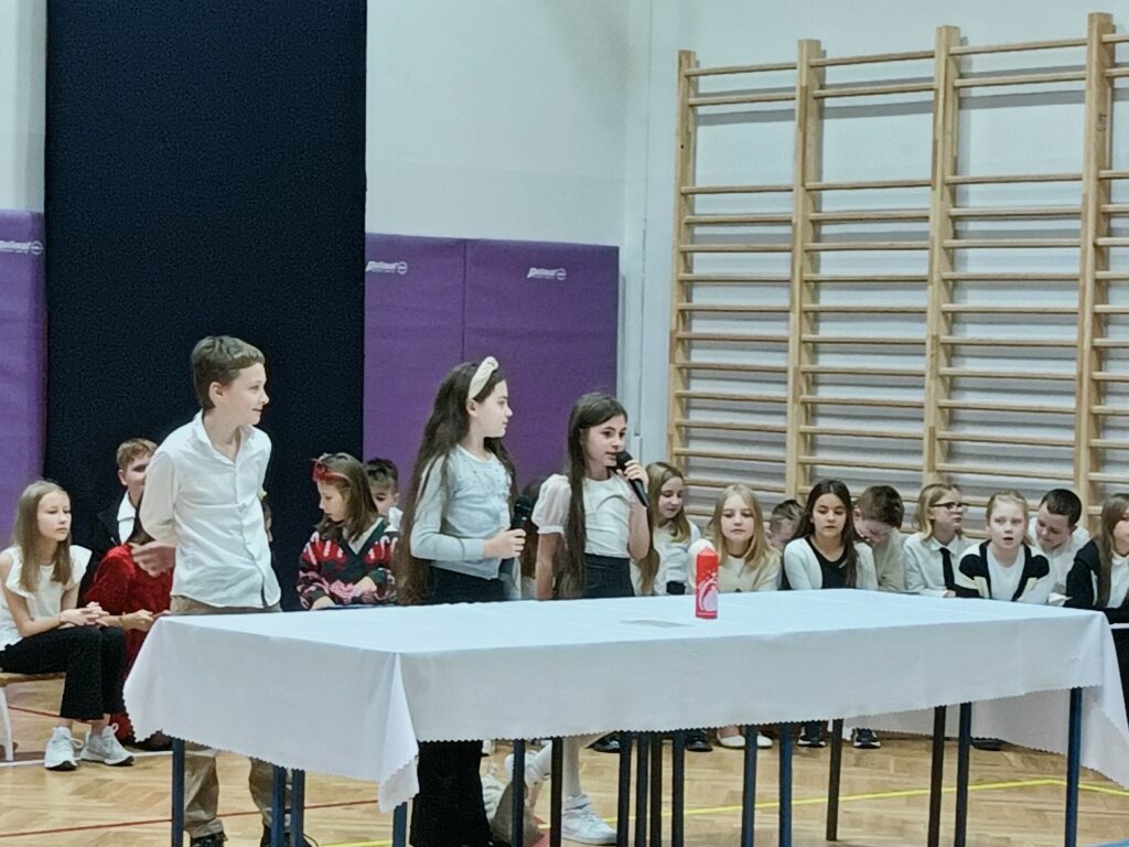 dwie uczennice stoją przy stole z białym obrusem na scenie