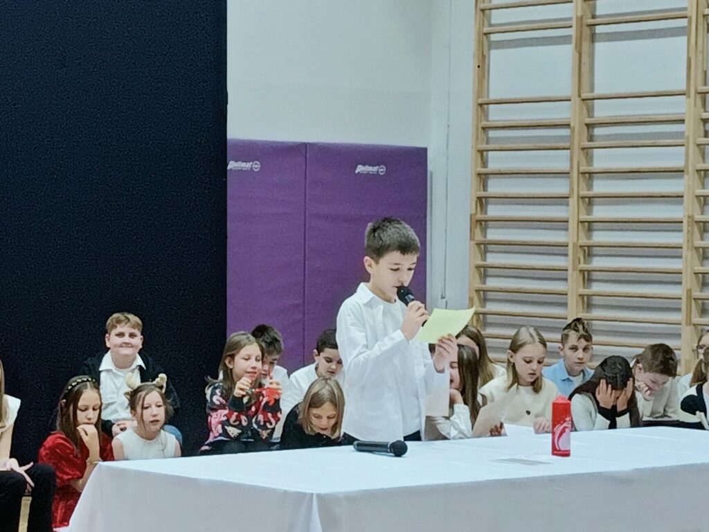 uczeń czyta z kartki przy stole z białym obrusem na scenie