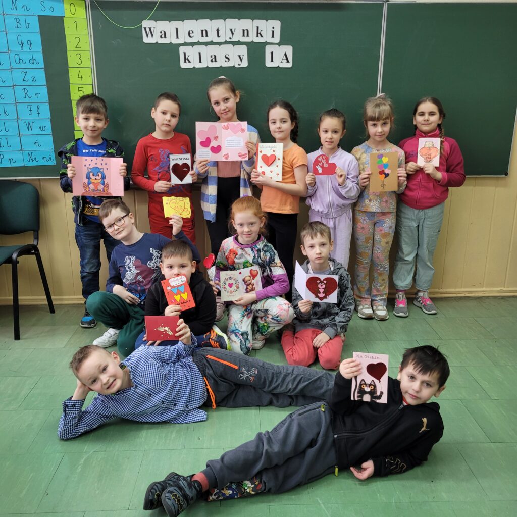 zdjęcie grupowe uczniów na tle ściany z napisem Walentynki klasy 1a