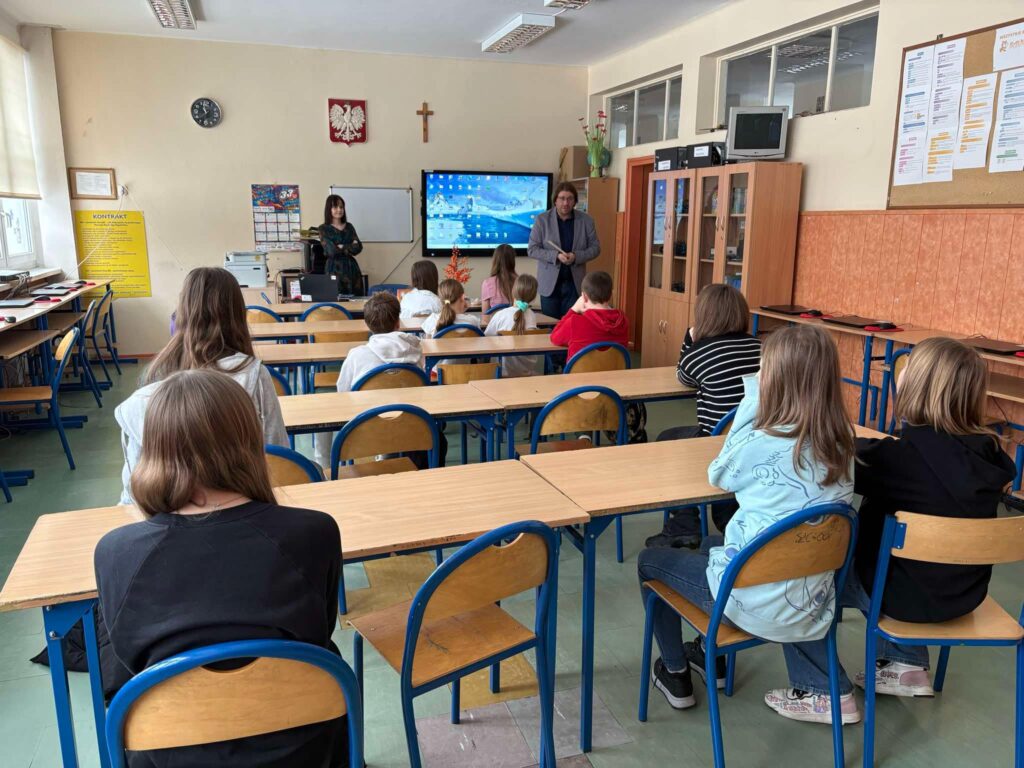 Dyrektor przemawia do zgromadzonych uczniów siedzących w ławkach