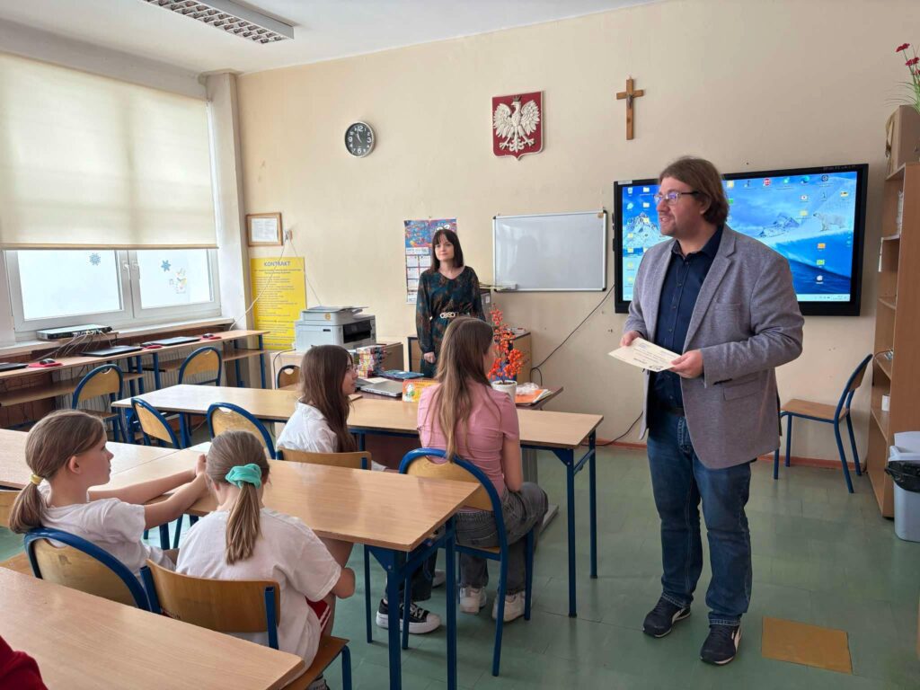 Dyrektor przemawia do zgromadzonych uczniów siedzących w ławkach